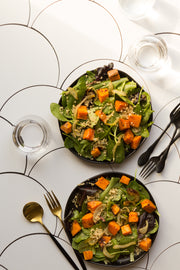Two green salads on black plates on a diagonal with Scalloped Tiles Replica Photography Backdrop