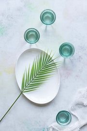 Palm leaf on a plate with glasses and white linen on subtle pastel backdrop